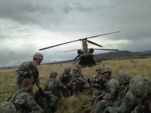 A group of 12 Buffalo Battalion cadets wait in the middle of a field to board the Chinook Helicopter in the background
