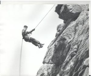 A black and white photo for a former ROTC cadet rappelling down a rock face.)