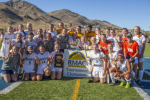 The Mines women's soccer team poses on the field with a flag announcing their RMAC tournament championship win.