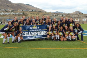Mines women's soccer team holds a championship banner on the soccer field