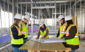 Construction engineering students and a faculty member review a blueprint on a construction site