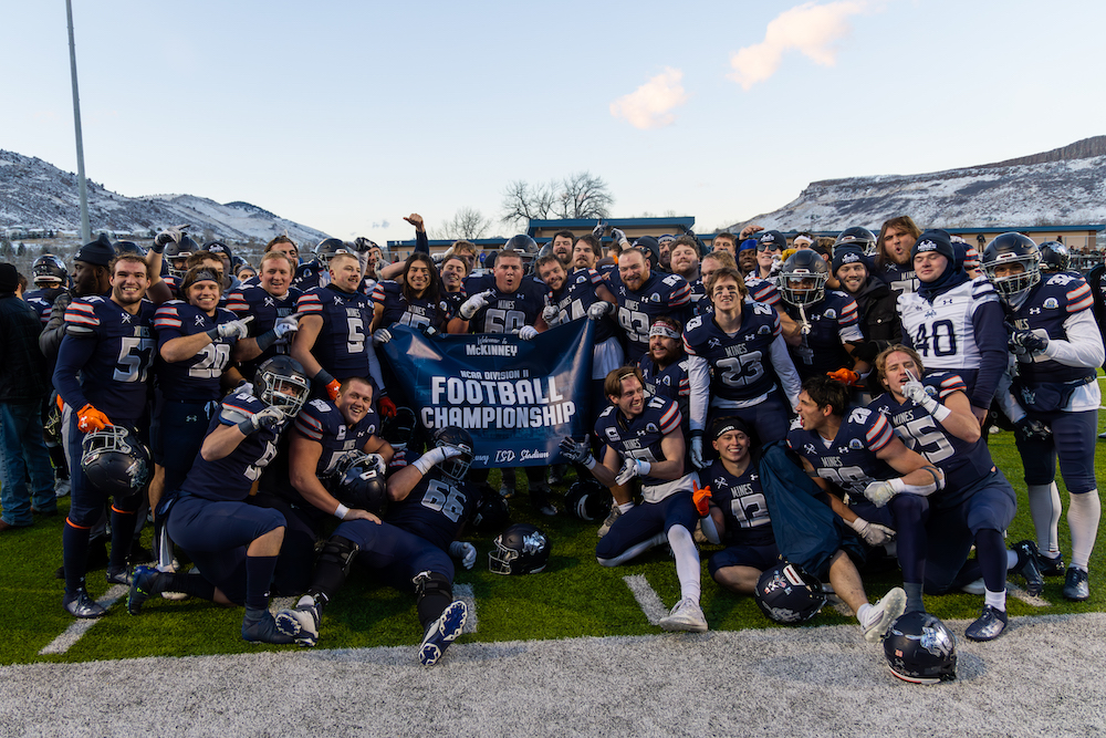 The Mines football team holding a NCAA Division II Football Championship banner.