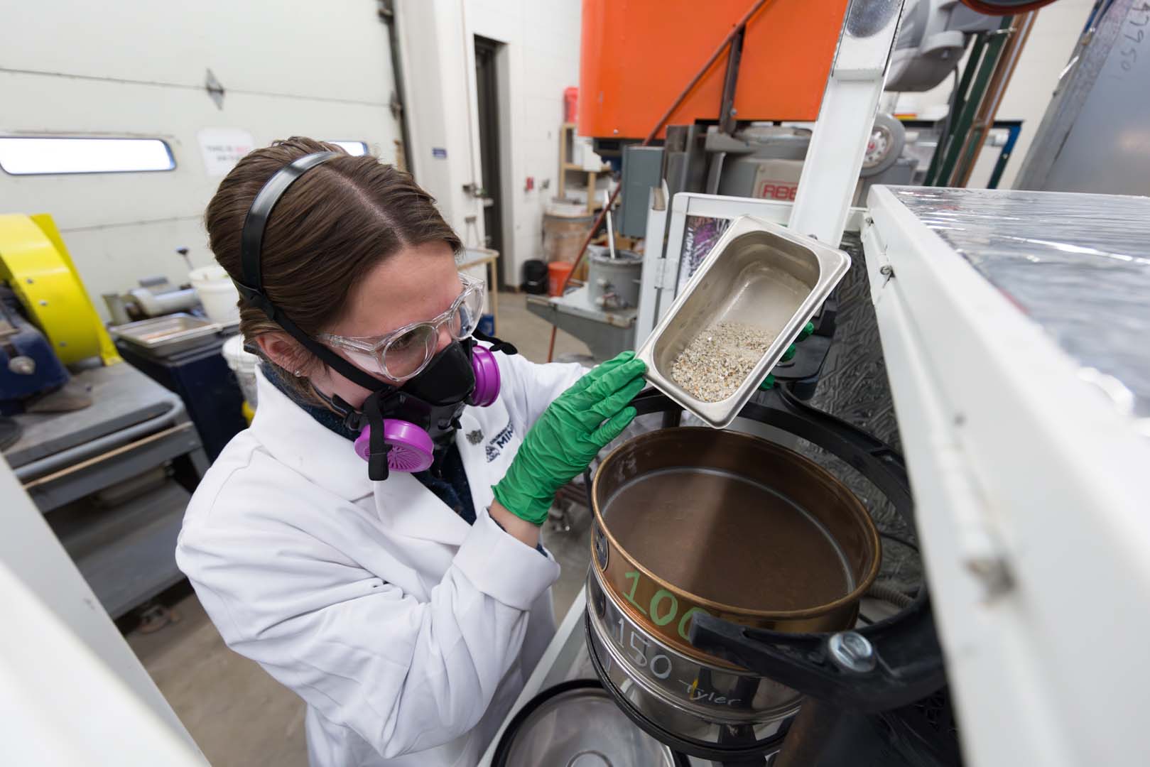 Karlie Haddon wears a respirator in a lab on the Mines campus and pours a sample into a RO-tap machine